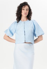 Lyseblå cropped jakke med teksturert stoff, pufferm, og rund halslinning, med en frontlukkning med knapper og en rett fald.