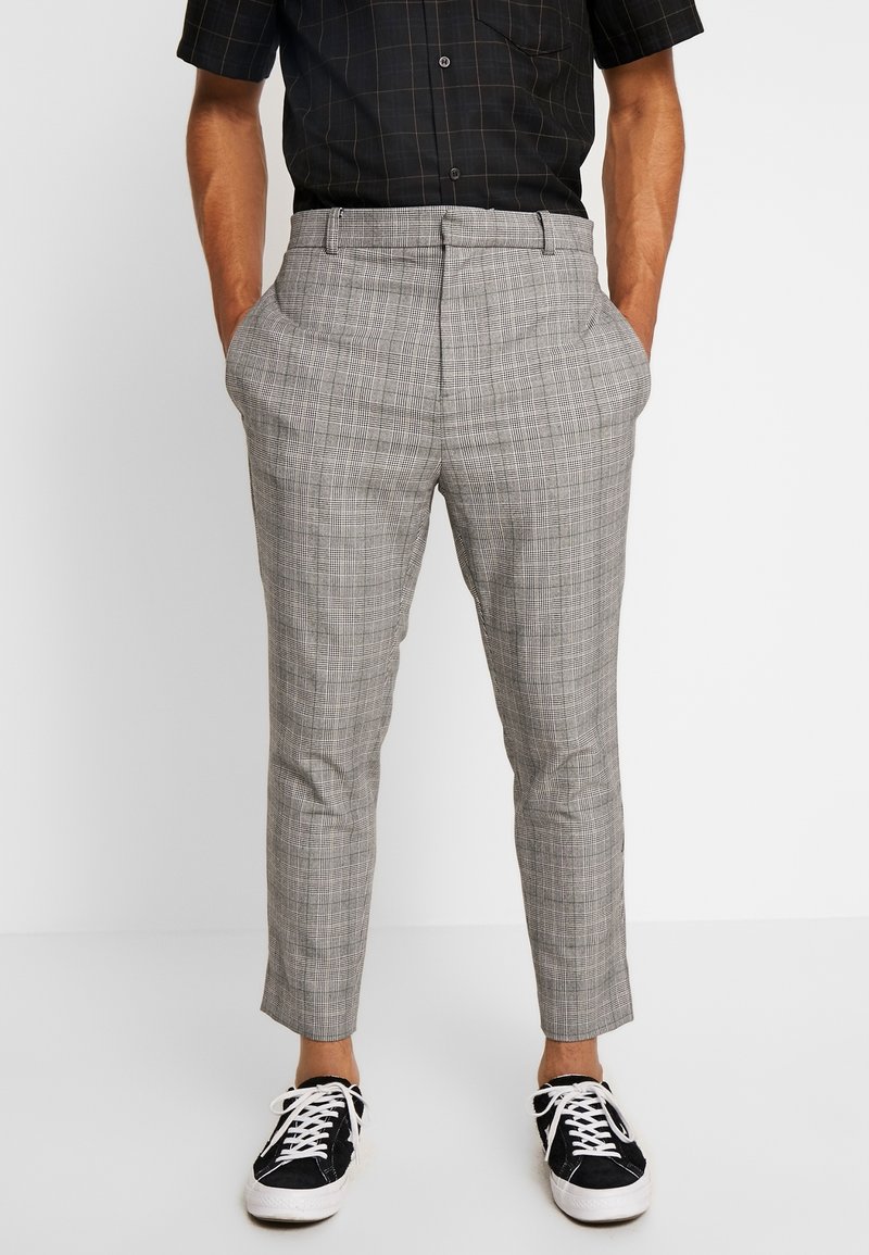 Pantalon à carreaux gris avec une coupe ajustée, doté de poches latérales et d'une taille mi-haute. Associé à des baskets noires pour un look décontracté.