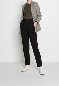 Czarne spodnie o zwężanym kroju zestawione z marynarką w jodełkę. Do tego prążkowany oliwkowy top i białe tenisówki, z subtelnymi wzorami.