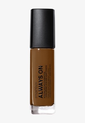 Flacon de fond de teint liquide Smashbox Always On en teinte marron foncé avec un bouchon noir sur fond blanc.