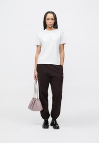 Λευκό βαμβακερό T-shirt με ανάγλυφο λογότυπο, συνδυασμένο με σκούρο καφέ φόρμες και τσαντάκι με κορδόνι σε ανοιχτό μωβ χρώμα. Μαύρα γυαλιστερά παπούτσια ολοκληρώνουν την εμφάνιση.