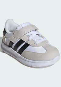 Biele športové tenisky s šedými semišovými akcentmi, čiernymi pruhmi a dizajnom na šnurovanie. Suchý zips pre bezpečné uchytenie, textúrovaná podrážka pre lepšiu priľnavosť.