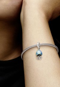 Srebrna zapestnica z iridescentnim čarom meduze in dvema kamenčkoma, na strukturirani vezi, nosena na goli roki.