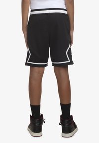 Zwarte sportshorts van mesh-stof, met witte accenten en een rekbare tailleband. Draag ze met zwart-rode hoge sneakers.