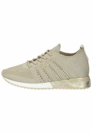 Beige athletic shoe with knit upper, round toe, lace-up front, textured surface, and a contrasting shiny heel accent.