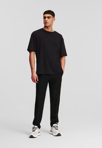 Fekete, nagyméretű póló rövid ujjakkal, a mellrészen egy diszkrét logóval. Fekete, slim fit nadrággal és fehér tornacipővel párosítva.