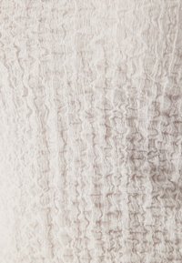 Tessuto leggero con un motivo stropicciato in toni beige morbidi. Il materiale appare leggero e flessibile.