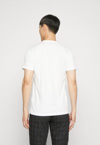 Bílá krátká trička s krátkým rukávem a kulatým výstřihem, vyrobené z bavlny, zobrazené zezadu, s hladkou texturou a minimalistickým designem.