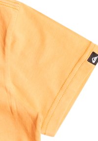 Oranžové bavlněné tričko s krátkým rukávem. Má prošívaný lem a černou nášivku s logem na rukávu. Měkká textura a ležérní střih.