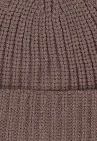 Beanie lavorato a maglia in morbido tessuto a coste con un colore mauve tenue. Presenta un risvolto nella parte inferiore per un ulteriore comfort e calore.