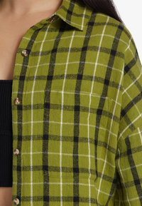 Zielonoczarny flanelowy kosz shirt z kołnierzykiem zapinanym na guziki, charakteryzujący się teksturowanym materiałem i kontrastowymi białymi liniami w kratkę.