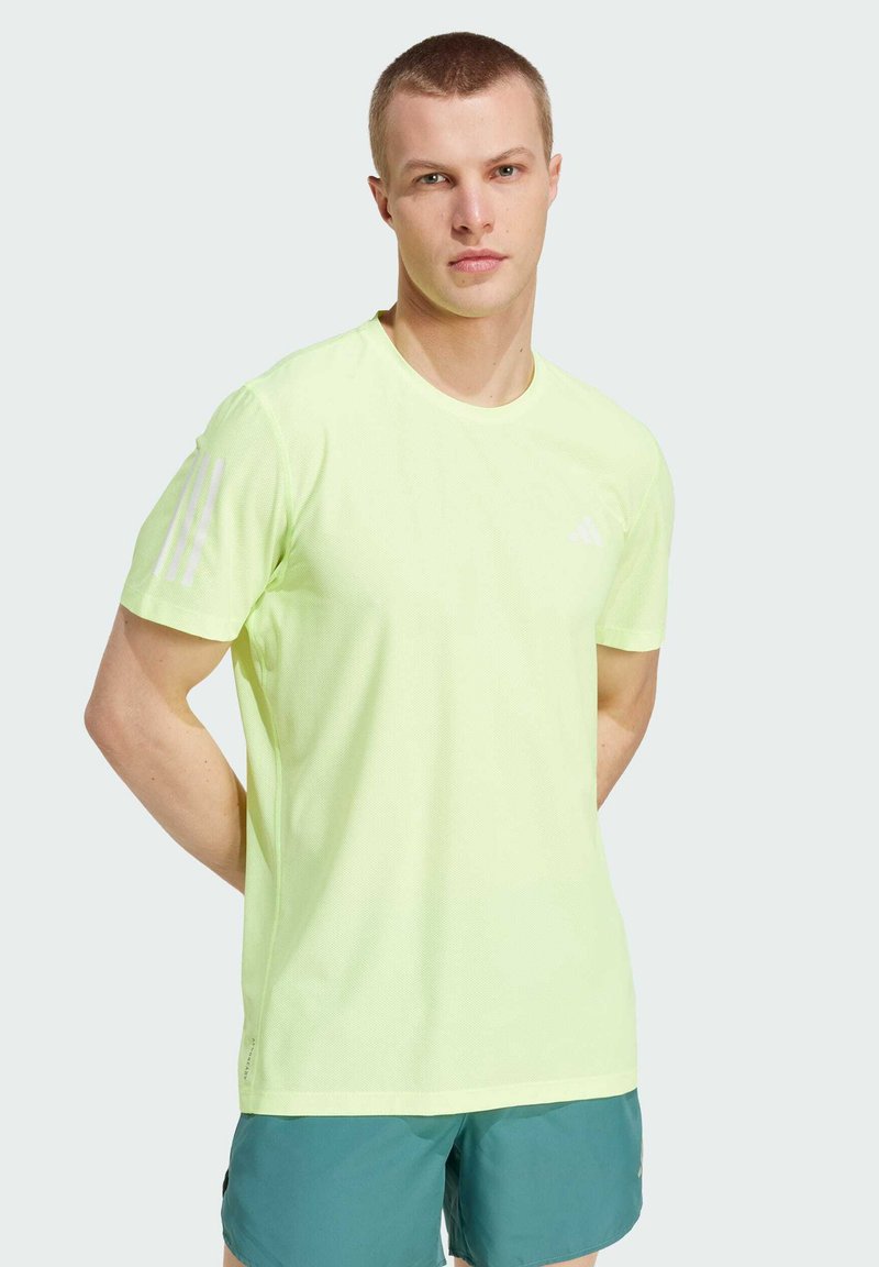 Camiseta deportiva de color amarillo neón, con manga corta, cuello redondo y tres rayas blancas en el hombro izquierdo. Tela ligera y transpirable.