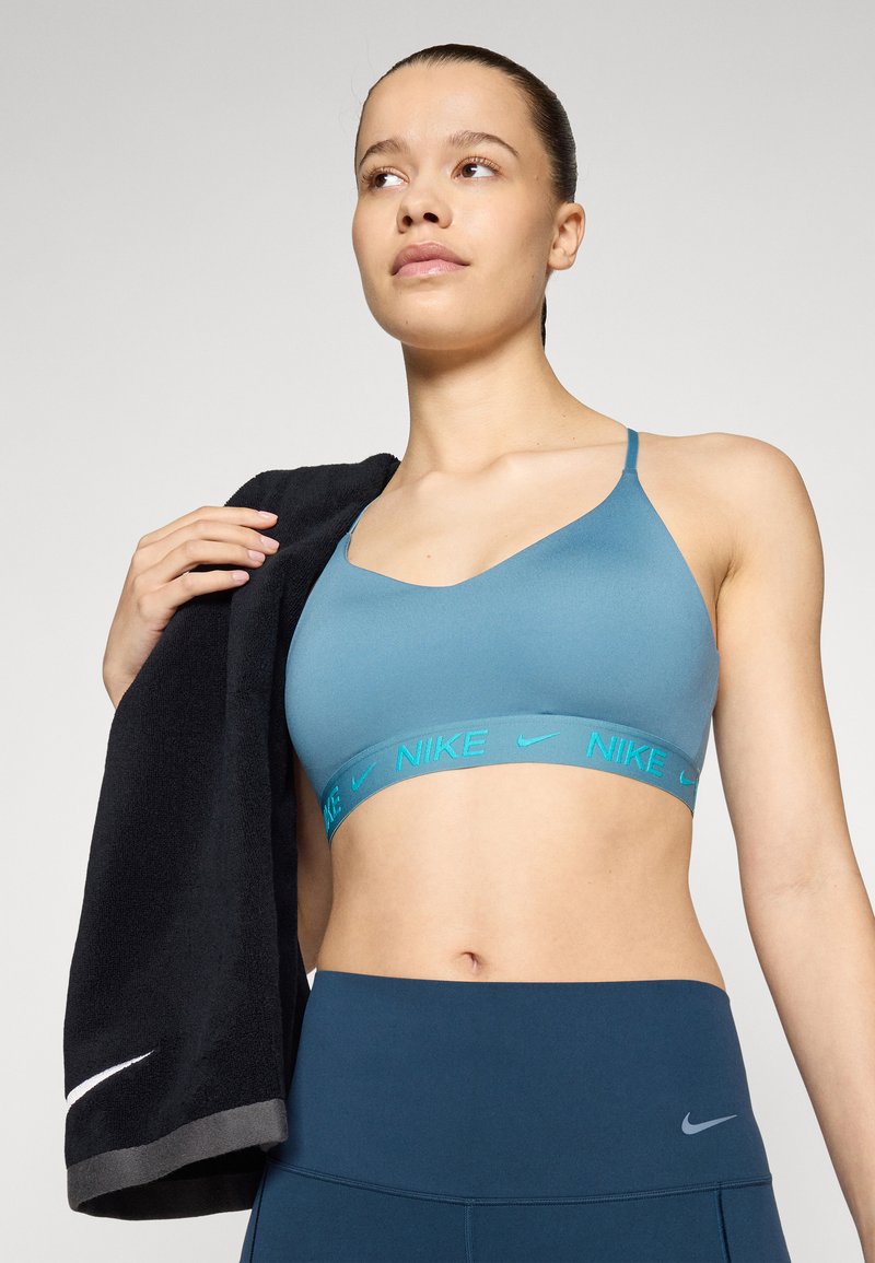 Sujetador deportivo azul claro con una cintura ancha que presenta "NIKE" en turquesa, combinado con leggins de talle alto azul oscuro y una toalla negra.