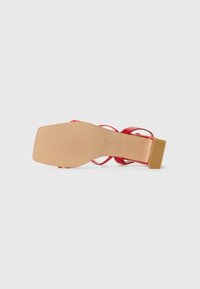Red high-heeled sandal with a chunky heel, transparent straps, and a beige sole featuring textured grip patterns.