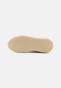 Semelle en caoutchouc de sneaker de couleur beige clair, présentant des stries horizontales pour une meilleure adhérence et un bout arrondi. Logo embossé sur le côté.