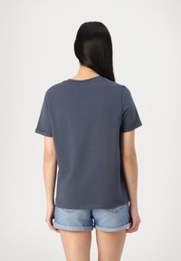 Marineblauw T-shirt met korte mouwen en een ronde hals, gemaakt van katoen, met een relaxte pasvorm en opgerolde mouwen. Ggedragen met denim shorts.