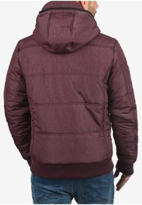 Burgunderfarget puffjakke med hette, med en teksturert overflate, ribbede mansjetter og nederkant, samt stitch-detaljer over ryggen.