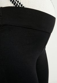 Leggings negros de talle alto, hechos de material elástico, con una textura suave y sin patrones visibles ni detalles de herrajes.