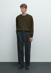 Dunkelolivgrünes Langarmhemd, graue Crew-Neck-Schicht, kombiniert mit hochtaillierten, schwarzen plissierten Hosen und schwarzen Schuhen.