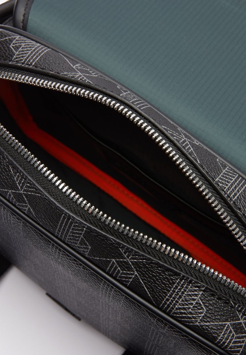 Schwarzer Rucksack mit strukturiertem Gewebe und geometrischem Muster, silbernem Reißverschluss und rotem Innenfutter, teilweise geöffnet, um die inneren Fächer zu zeigen.