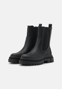 Botines negros de tobillo con un acabado de piel suave, paneles laterales elásticos y una suela de goma gruesa que presenta un patrón de textura en la banda de rodadura.