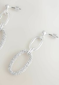 Stříbrné visací náušnice se dvěma propojenými oválnými tvary, větší ovál posetý průhlednými kamínky, uzavření na šroubový podklad.