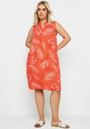 Ärmelloses orange Kleid mit weißem Blattmuster, V-Ausschnitt und knielangem Saum. Getragen mit weißen Sandalen.