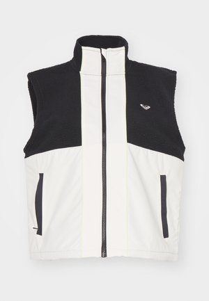Chaleco sin mangas en blanco y negro con un alto cuello, cierre de cremallera, textura de forro polar y bolsillos laterales; cuenta con costuras en contraste y un logo.