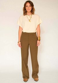 Haut crème à manches courtes avec une coupe ample, associé à un pantalon large marron bien ajusté et des chaussures à bout pointu couleur tan. Les accessoires comprennent des colliers superposés et un bracelet.