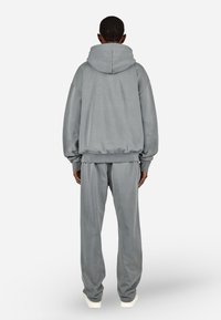 Sweatshirt cinzenta com capuz grande, ombros caídos e bainha canelada, combinada com calças de treino do mesmo tecido. Textura suave, corte solto.