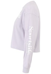 Lila pitkähihaine croptop, valmistettu pehmeästä puuvillasta. Oikeassa hihassa on valkoista painettua tekstiä "Sportslife". Pyöreä kaula-aukko ja resorikainalot.