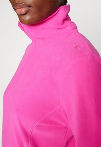 Růžový mikinový pulovr s vysokým límcem, polovičním zipem a decentním logem na rameni. Hladká textura a přiléhavý střih.