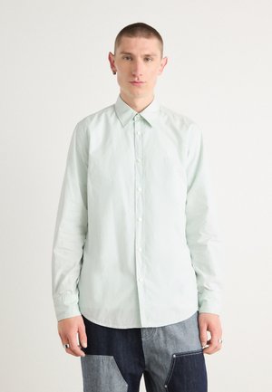 Chemise à manches longues vert menthe clair avec un col boutonné, présentant une texture subtile et un petit logo sur la poitrine.