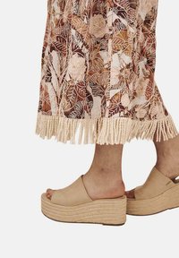 Las sandalias de plataforma beige presentan un diseño liso con una correa ancha y una suela texturada tejida. La falda tiene un patrón floral y un dobladillo con flecos.