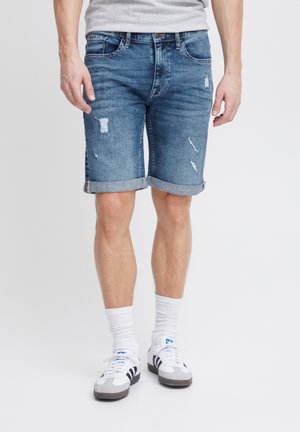 Denimshorts, ljusblå med slitna detaljer, fem fickor, uppvikta manschetter, matchat med vita strumpor och grå sneakers med svarta accenter.
