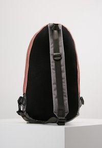 Vista posteriore di uno zaino realizzato in tessuto a rete nero, con accenti grigi e piping laterale rosa, dotato di spallacci regolabili e dettagli hardware.