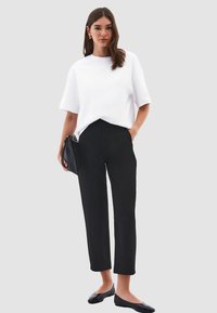 Witte, kortemouw t-shirt gecombineerd met high-waisted zwarte broeken, platte zwarte schoenen en een zwarte clutch. Minimalistisch ontwerp en kleurenpalet.