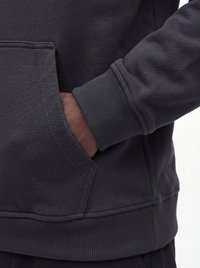 Main dans la poche d'un sweat-shirt gris foncé avec poignets et ourlet côtelés, montrant la texture du tissu et les détails des coutures.
