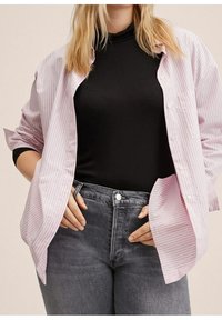 Camicia a righe rosa chiaro e bianca con maniche arrotolate sopra un dolcevita nero, abbinata a jeans scuri a vita alta.