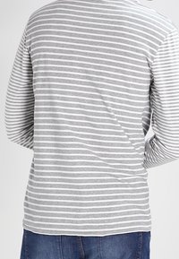 Camisa gris de manga larga con rayas horizontales blancas, con un escote redondeado y un corte relajado, combinada con jeans de mezclilla azules.