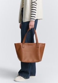 Brown leather tote bag with two sturdy handles, slightly curved top edge, pebbled texture, and no visible hardware accents.