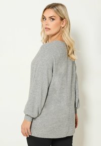Pull à manches longues en gris clair, fabriqué dans un matériau doux. Il présente un col rond et des manches amples, avec une coupe décontractée dans le dos.