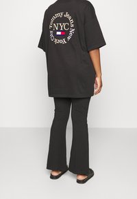 Czarna, oversize t-shirt z logo "Tommy Jeans NYC" na plecach, w połączeniu z czarnymi spódnicami w kształcie dzwonu i czarnymi sandałami, widok od tyłu.