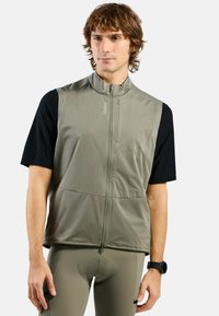 Figurbetonte aktive Weste in Olivgrün mit hohem Kragen, Frontreißverschluss und zwei Taschen, getragen über einem schwarzen Kurzarmoberteil.