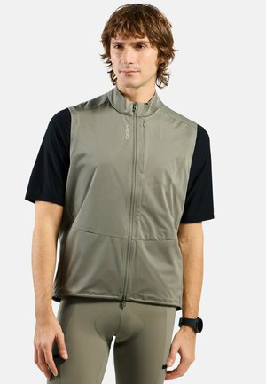 Fitted active vest in olive green, featuring a high collar, front zipper, and two pockets, worn over a black short-sleeve top.