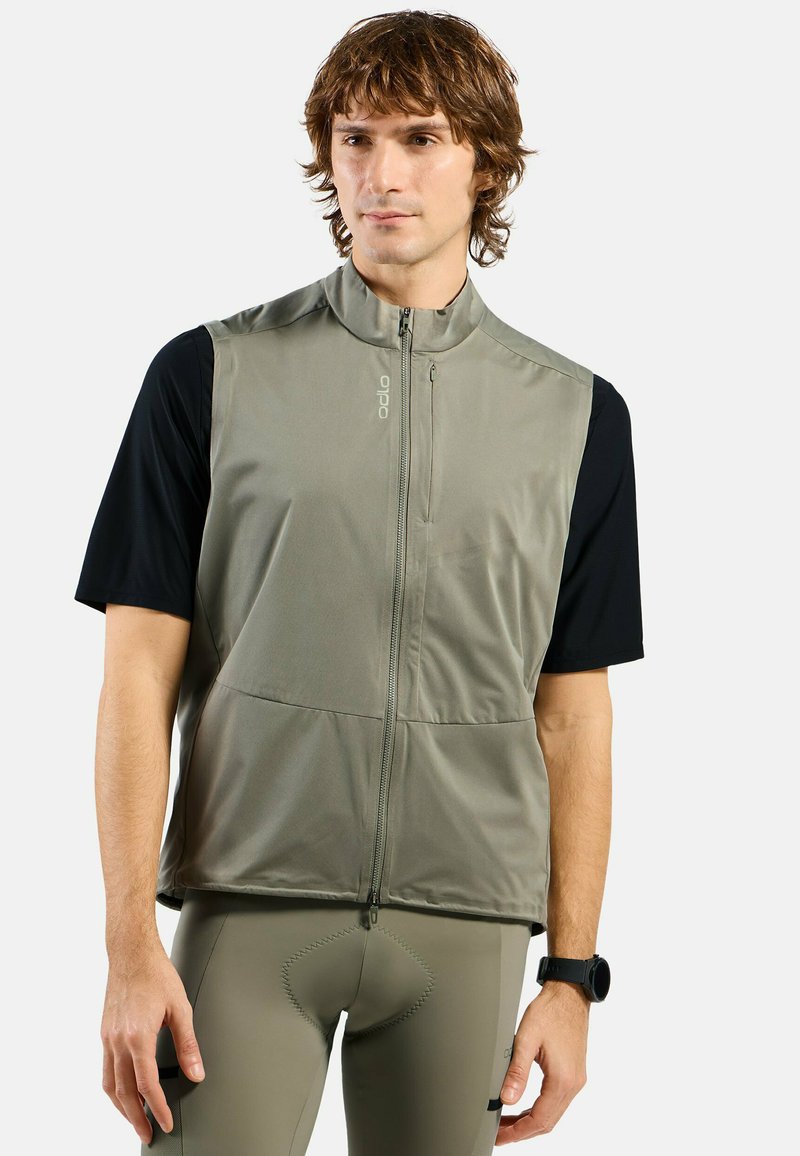 Figurbetonte aktive Weste in Olivgrün mit hohem Kragen, Frontreißverschluss und zwei Taschen, getragen über einem schwarzen Kurzarmoberteil.