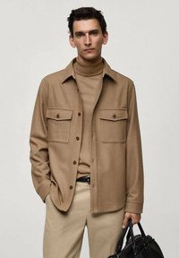 Bruine wollen blend overhemdjack met twee klepzakken, knoopsluiting en een zachte textuur, gedragen over een bijpassende coltrui en beige broek.