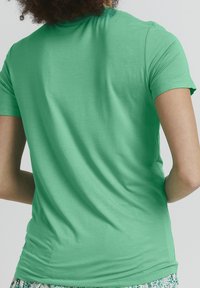 Grön kortärmad t-shirt i mjukt tyg. Har en figurnära passform med en slät yta och en enkel design utan dekorationer.