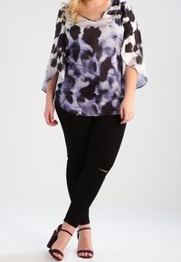 Blusa a fiori viola e nera fluida con maniche a campana, abbinata a jeans skinny neri strappati e tacchi a strappo viola.