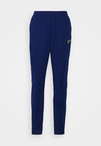 Sportieve marineblauwe broek van zachte stof, met een taps toelopend ontwerp en een klein neon groen Nike-logo aan de linkerkant.